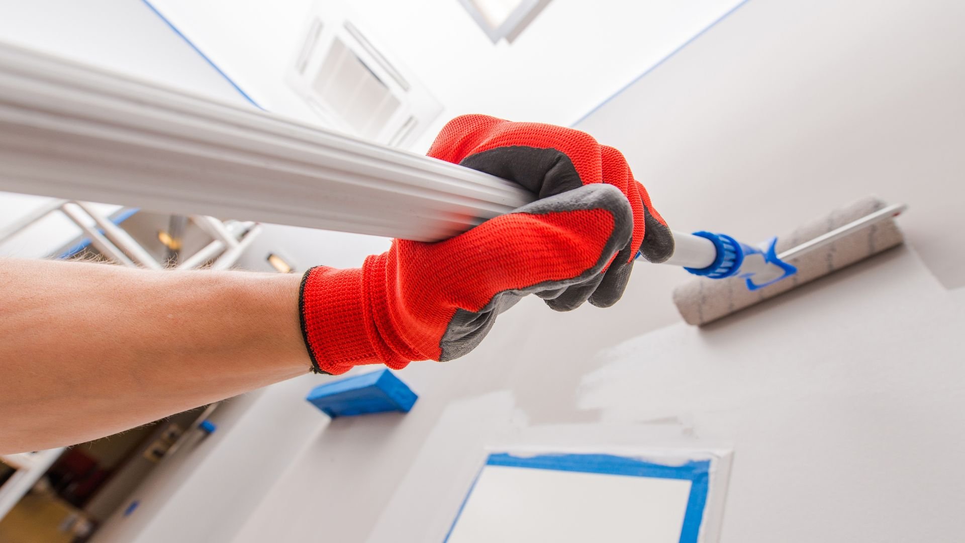 Hand in red glove painting wall with white paint roller