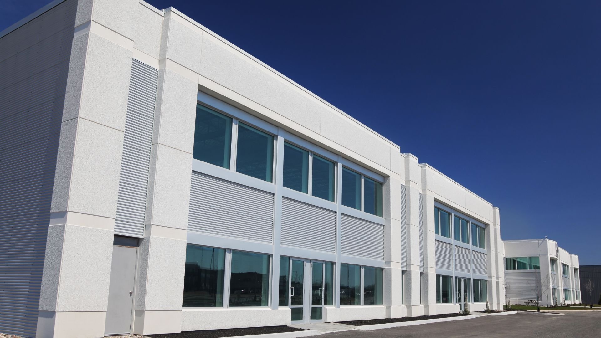 Modern white commercial building with large windows against blue sky