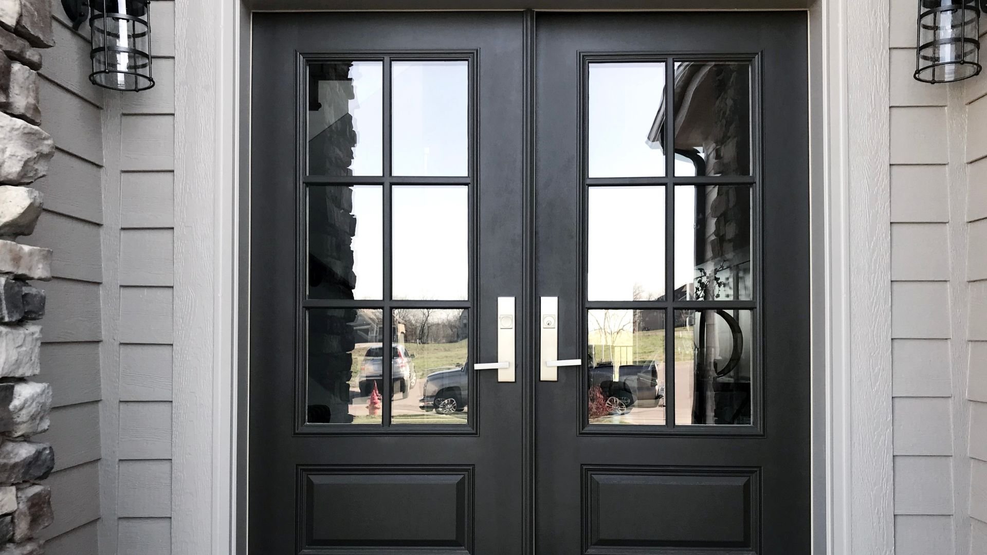 Black double front doors with glass panels reflecting neighborhood street